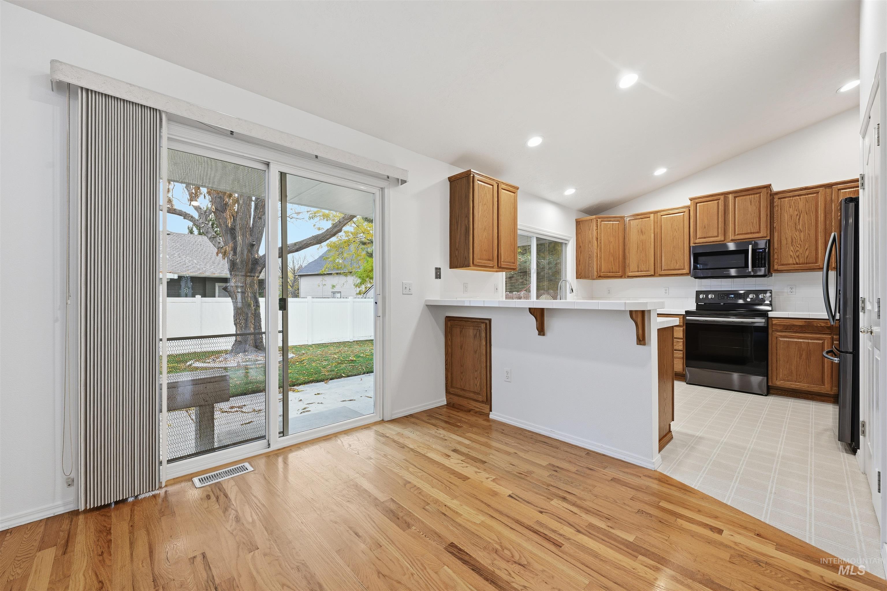 Kitchen featuring a kitchen bar, light countertops, a peninsula, black appliances, and lofted ceiling
