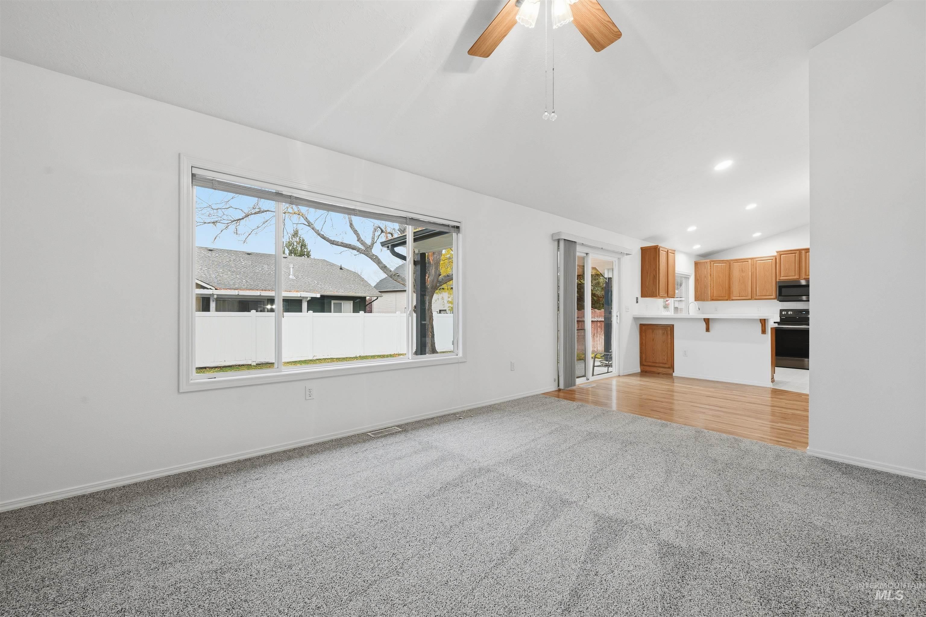 Unfurnished living room with light colored carpet, vaulted ceiling, a ceiling fan, and recessed lighting