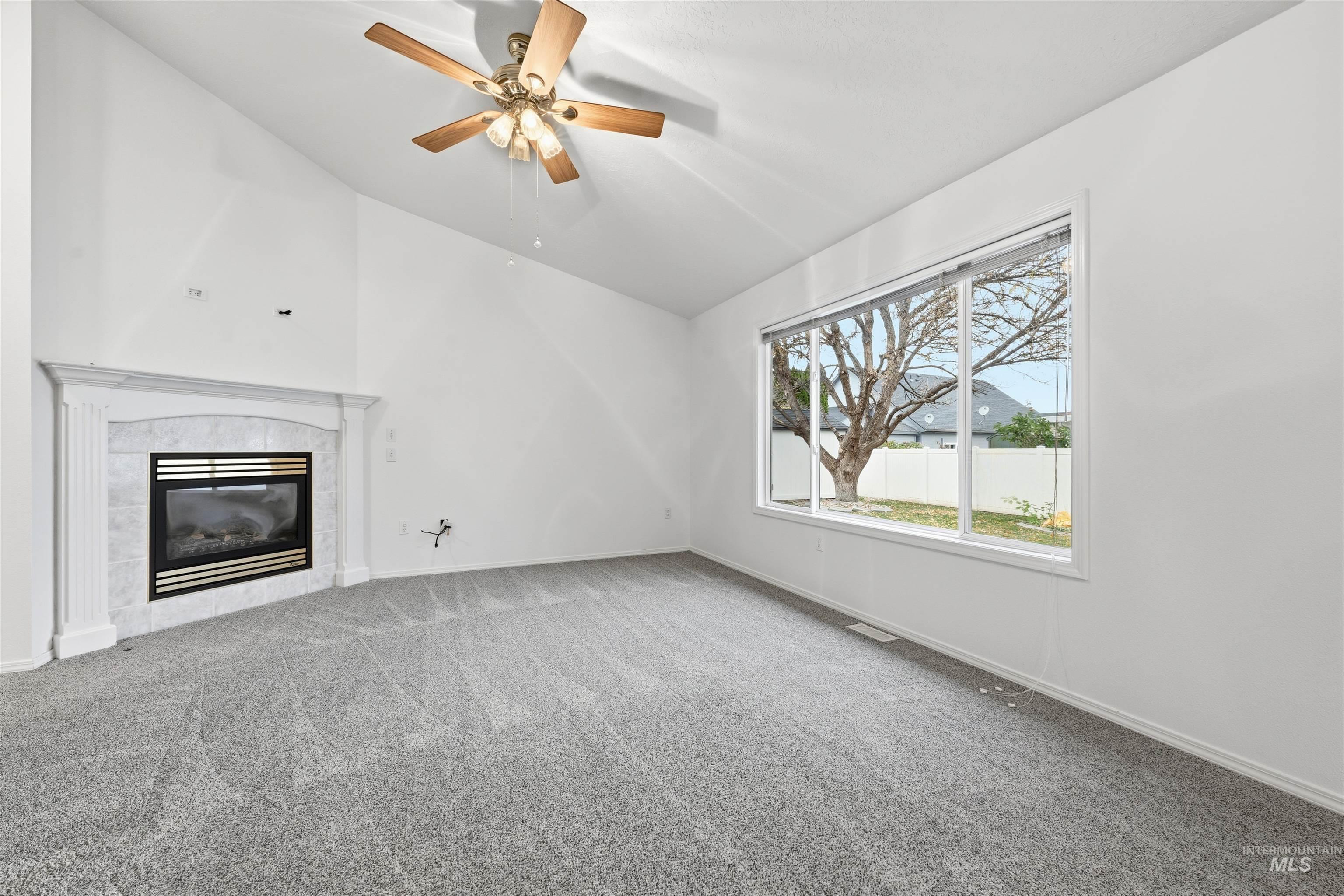 Unfurnished living room featuring vaulted ceiling, carpet floors, a tile fireplace, and a ceiling fan