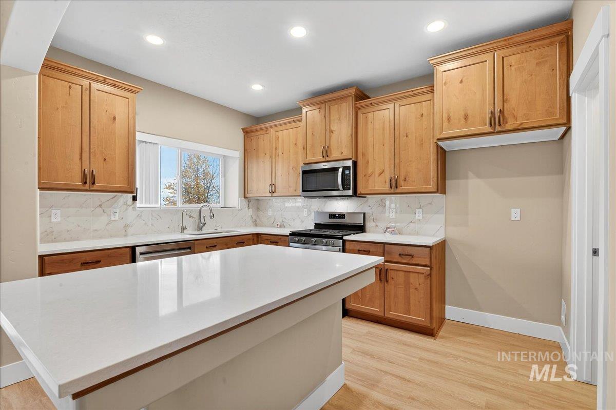 Kitchen featuring decorative backsplash, appliances with stainless steel finishes, light wood-type flooring, recessed lighting, and a kitchen island
