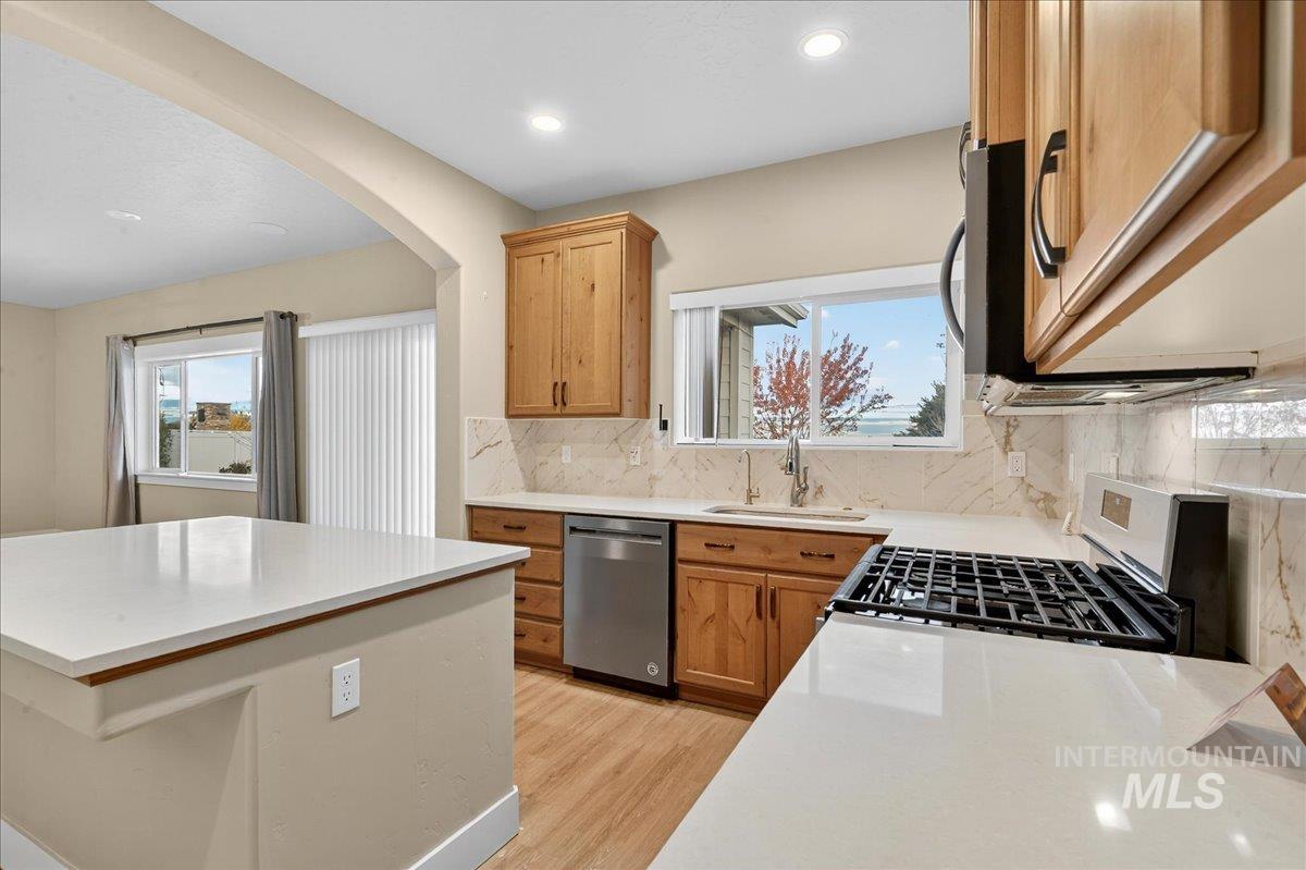 Kitchen featuring decorative backsplash, light wood-style floors, arched walkways, stainless steel appliances, and light stone countertops