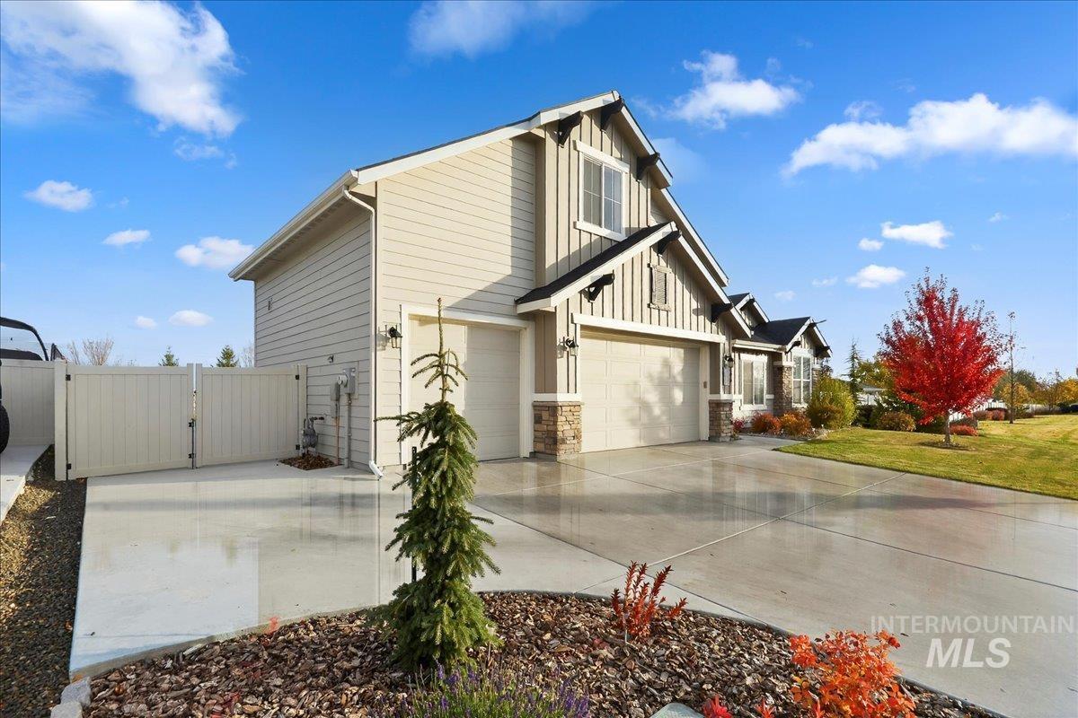 View of property exterior featuring board and batten siding, a gate, a garage, driveway, and stone siding