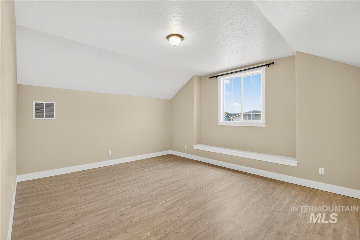 Additional living space featuring a textured ceiling, vaulted ceiling, and light wood-style flooring