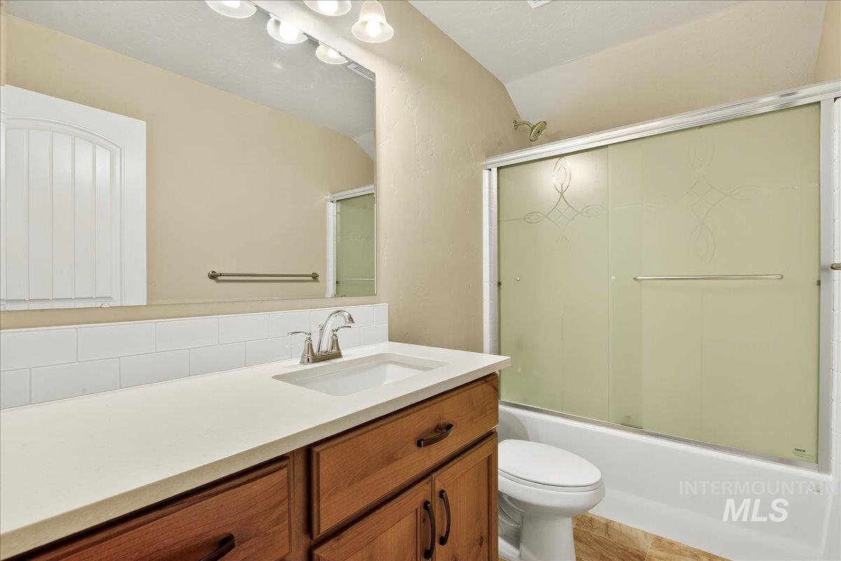 Full bath with vanity, bath / shower combo with glass door, and tasteful backsplash