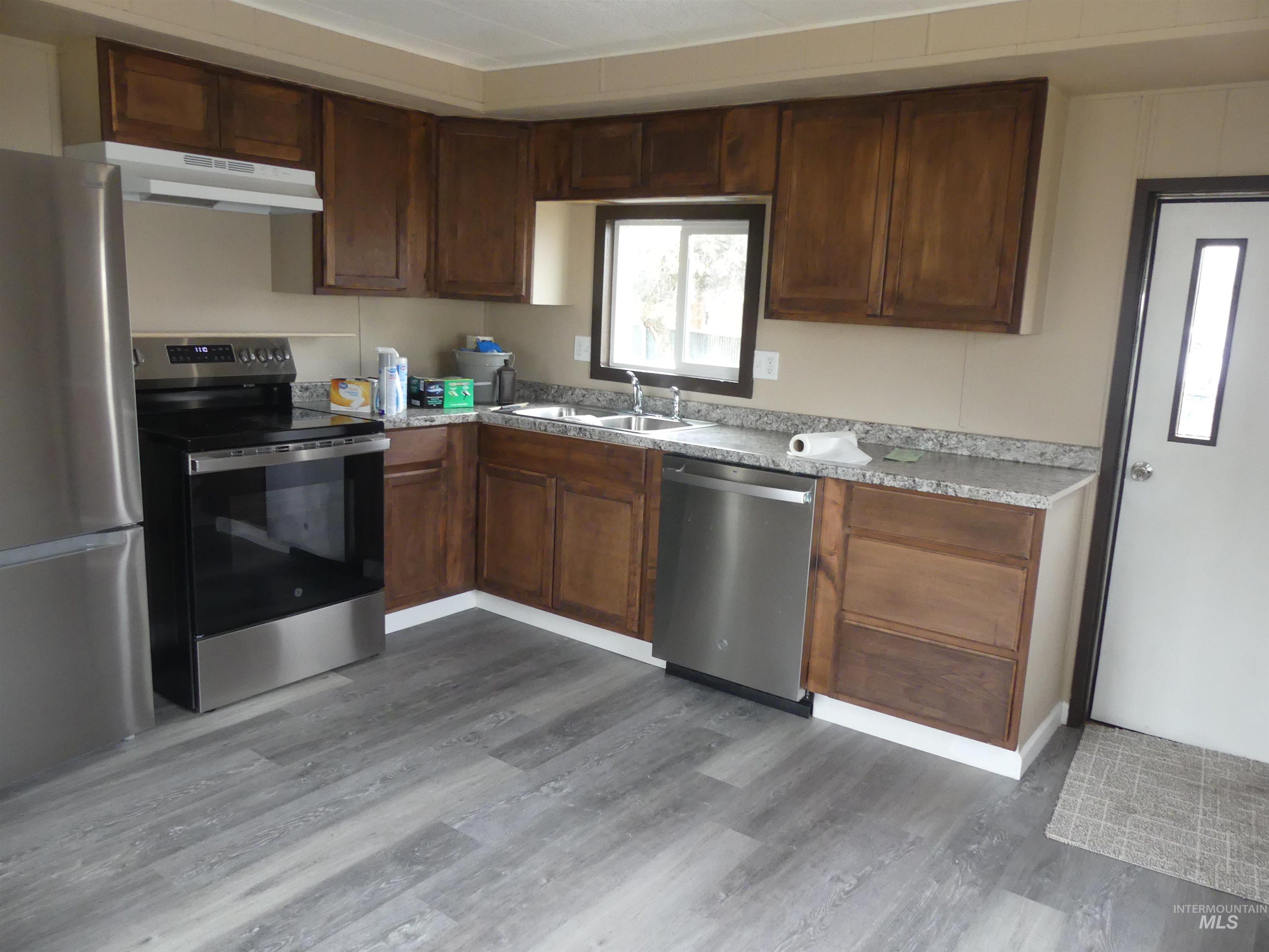 Kitchen featuring stainless steel appliances, light countertops, under cabinet range hood, and dark wood-type flooring