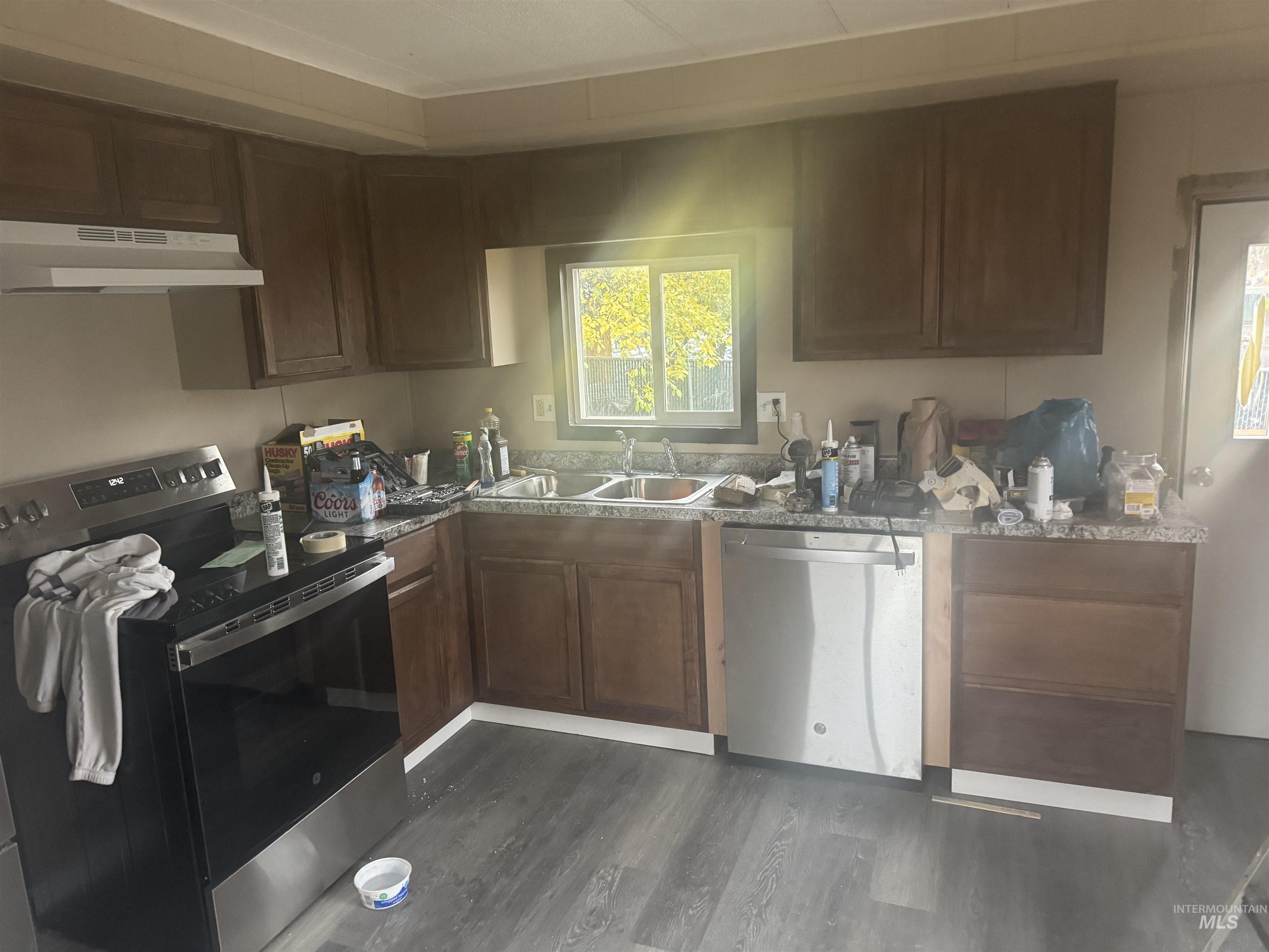 Kitchen featuring stainless steel appliances, under cabinet range hood, dark wood-style flooring, and dark brown cabinets
