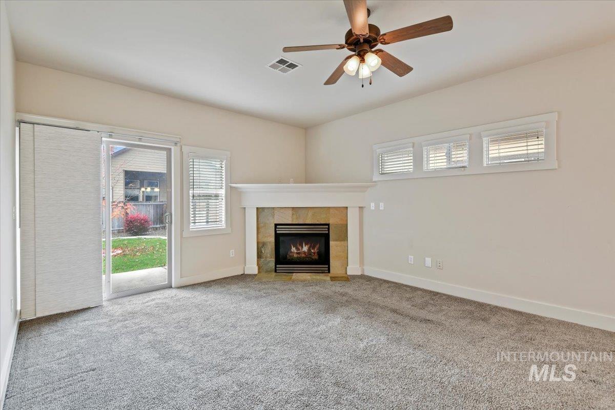 Unfurnished living room with healthy amount of natural light, carpet floors, a fireplace, and ceiling fan