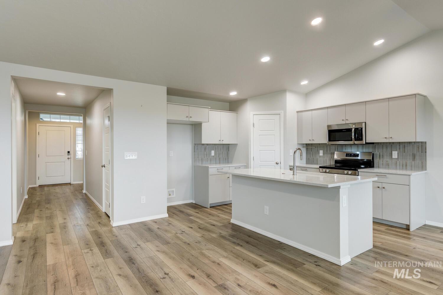 Kitchen with tasteful backsplash, recessed lighting, stainless steel appliances, a kitchen island with sink, and vaulted ceiling