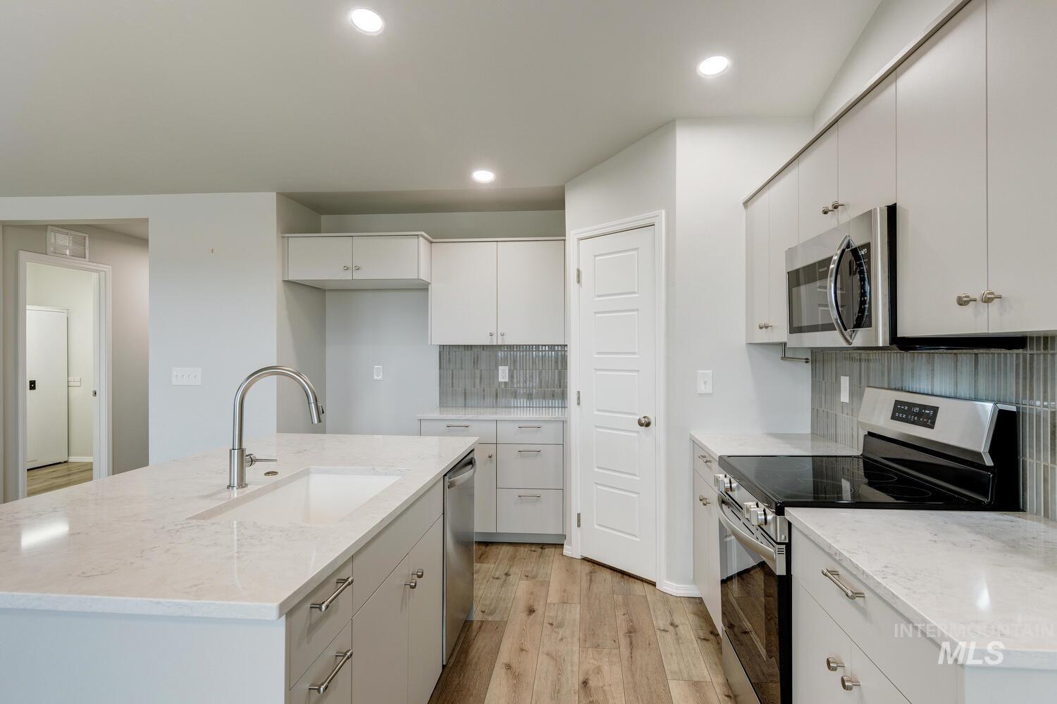 Kitchen with stainless steel appliances, light wood-style floors, light stone counters, a kitchen island with sink, and decorative backsplash