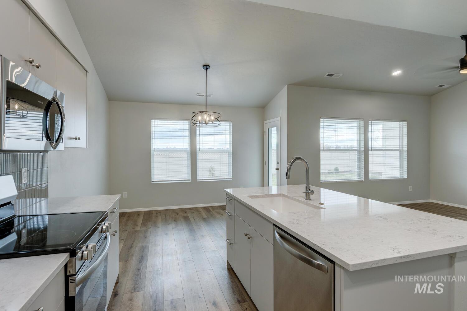 Kitchen with appliances with stainless steel finishes, white cabinets, light wood-style floors, pendant lighting, and light stone countertops