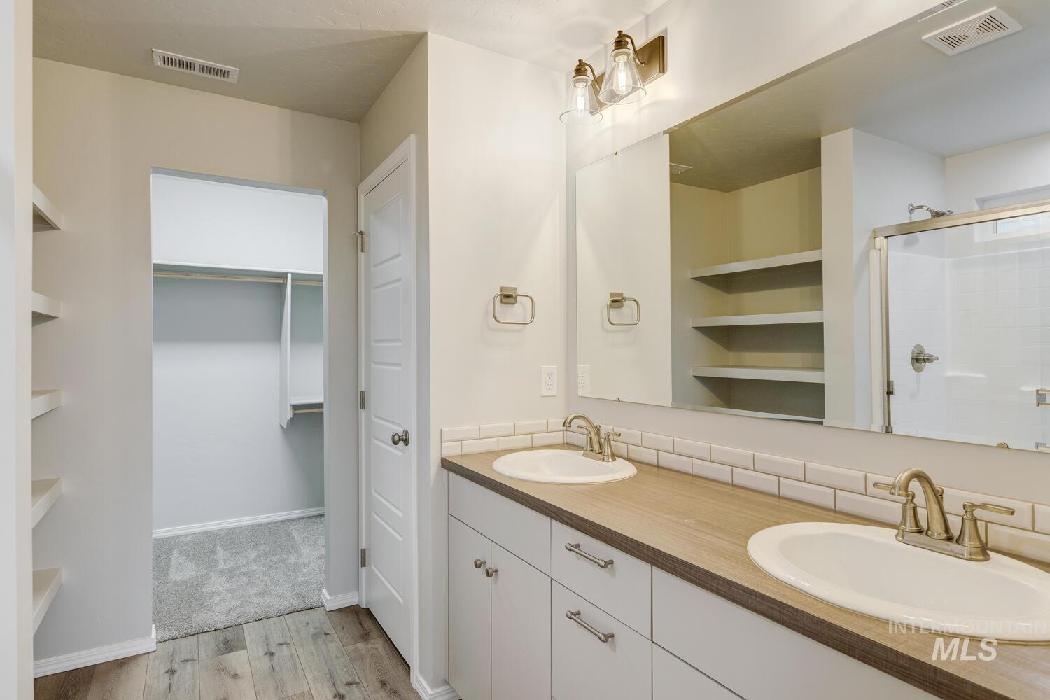 Full bathroom featuring light wood-type flooring, double vanity, a shower stall, and a walk in closet