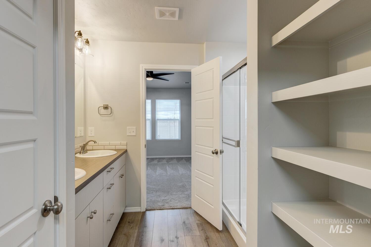 Full bathroom featuring double vanity, light wood finished floors, a stall shower, and a ceiling fan