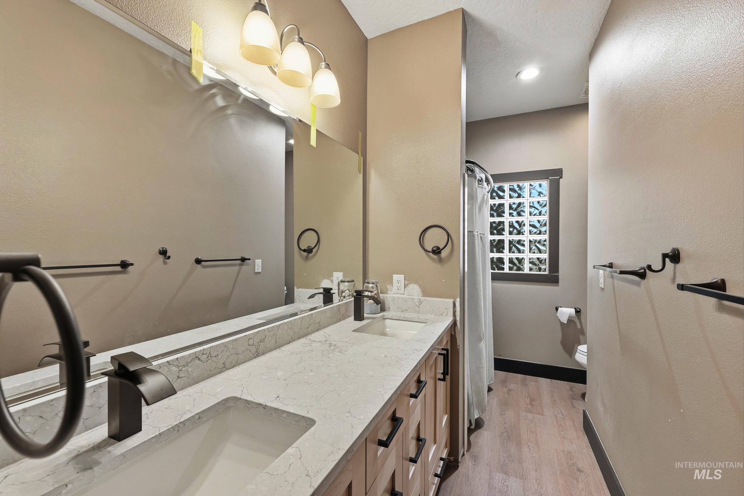 Full bath featuring double vanity, light wood-type flooring, and curtained shower