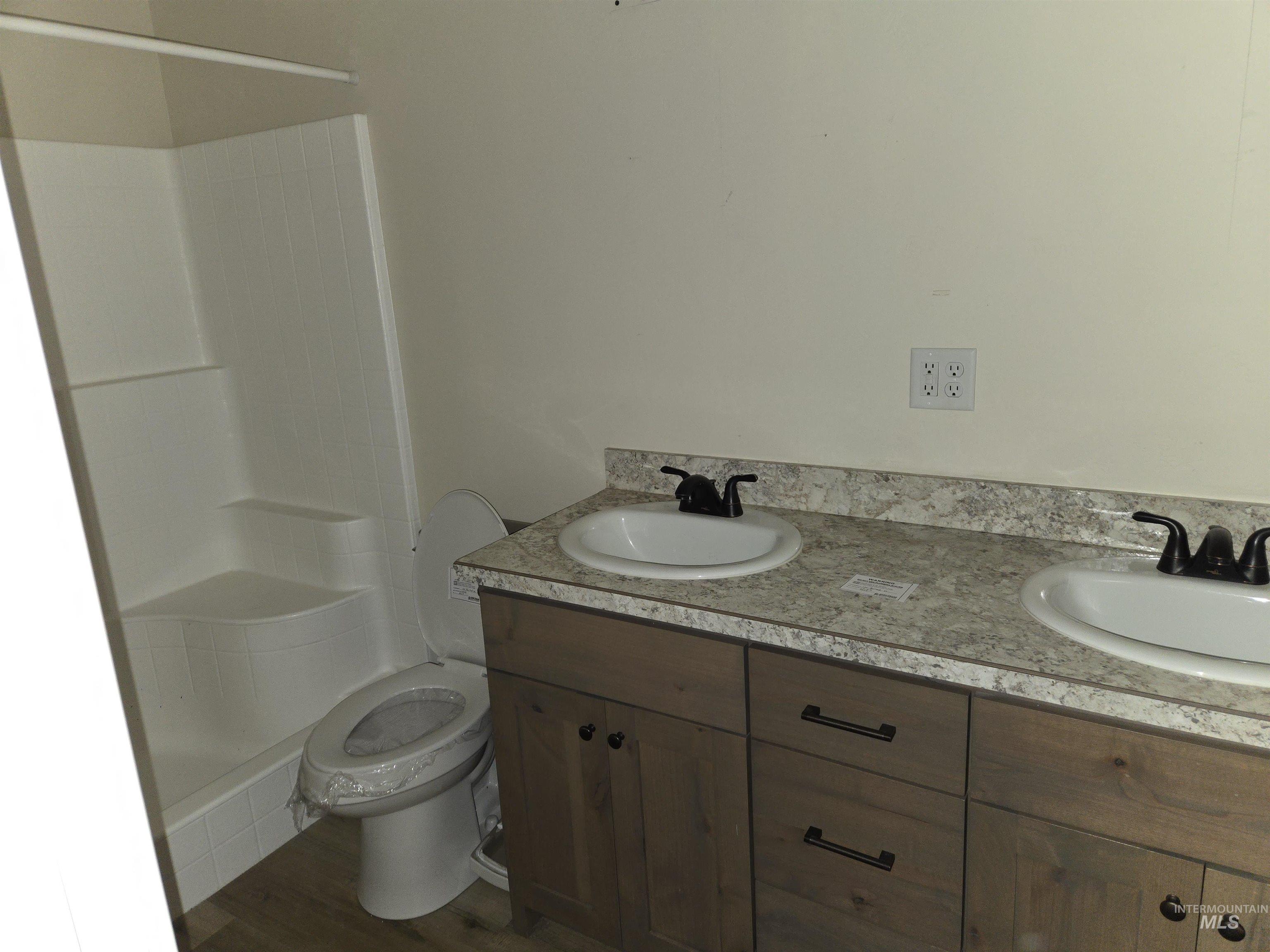 Bathroom featuring double vanity, a shower, and dark wood finished floors