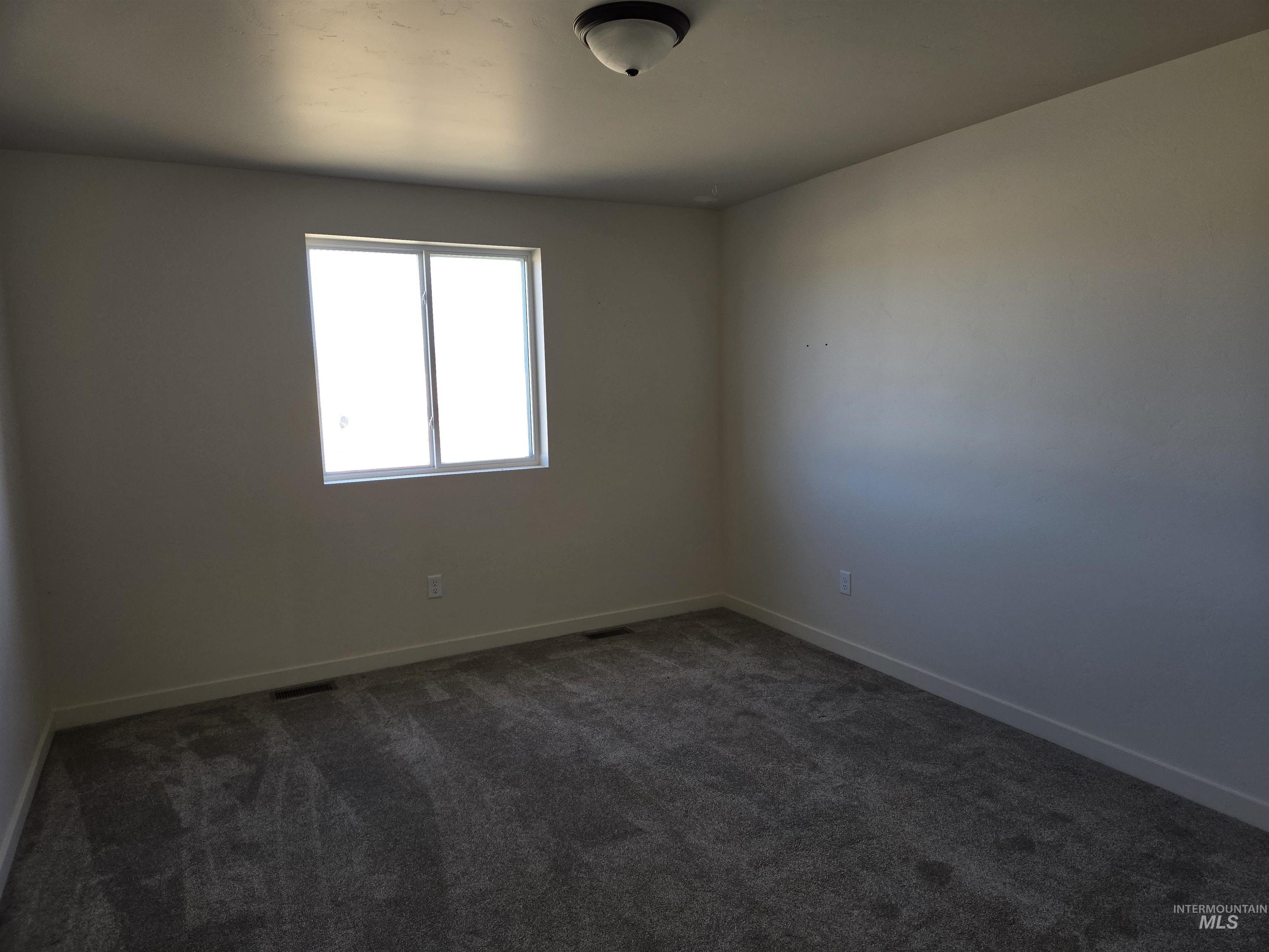 Empty room featuring dark carpet and baseboards