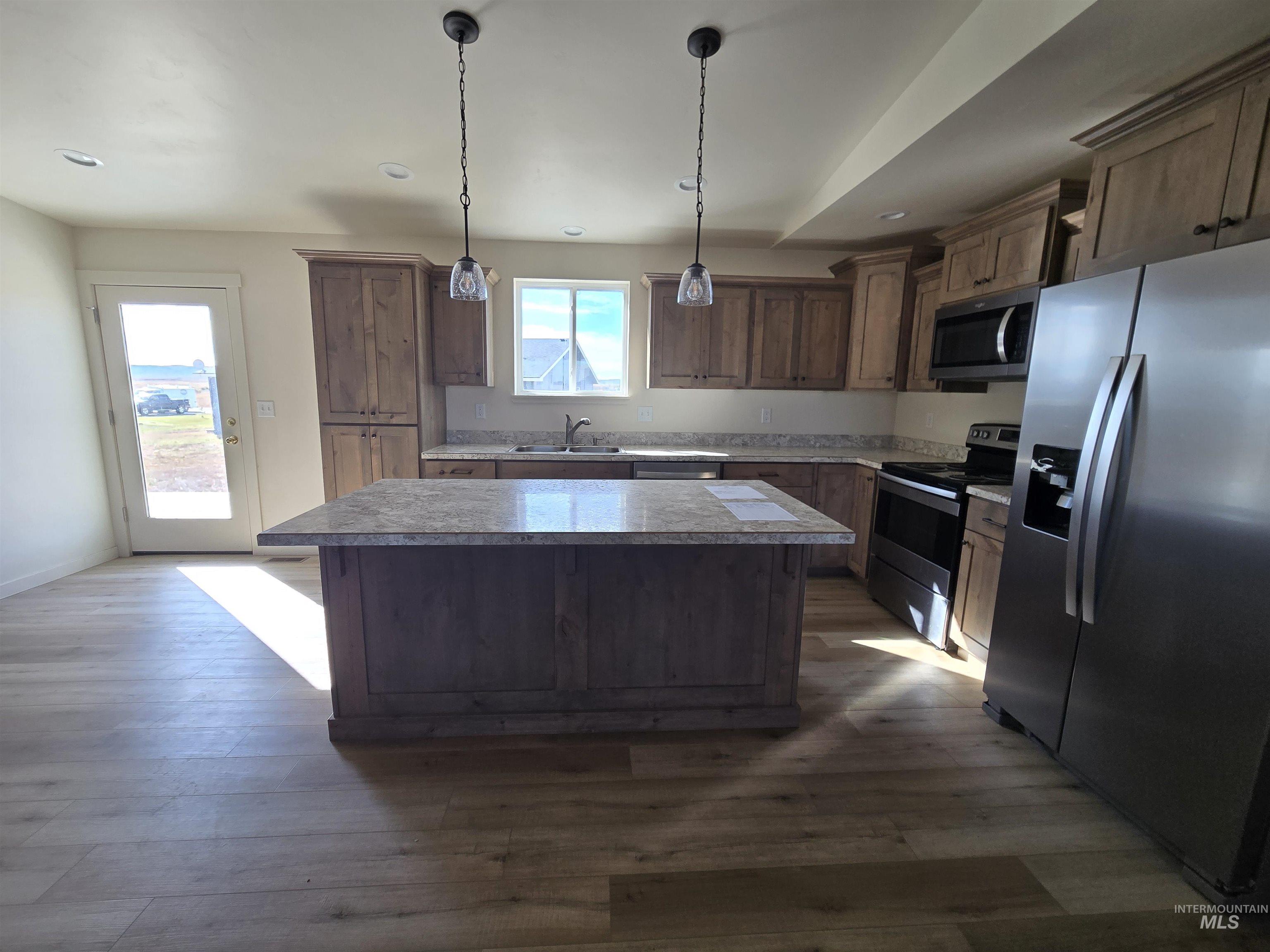Kitchen featuring stainless steel appliances, a kitchen island, decorative light fixtures, dark wood-style flooring, and recessed lighting
