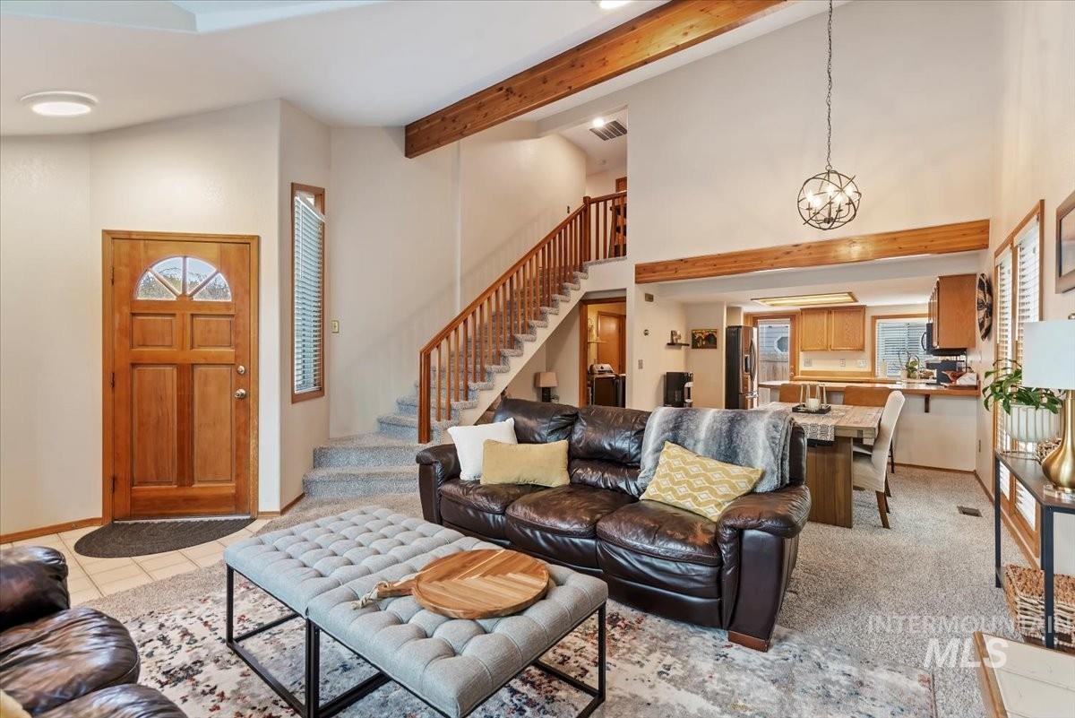 Living room featuring a high ceiling, beamed ceiling, stairs, a chandelier, and light tile patterned floors