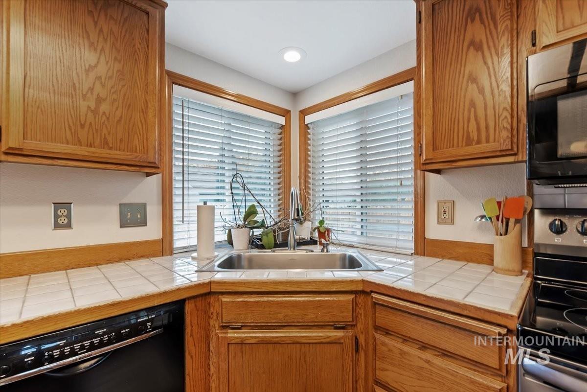 Kitchen with black appliances, tile counters, and brown cabinets