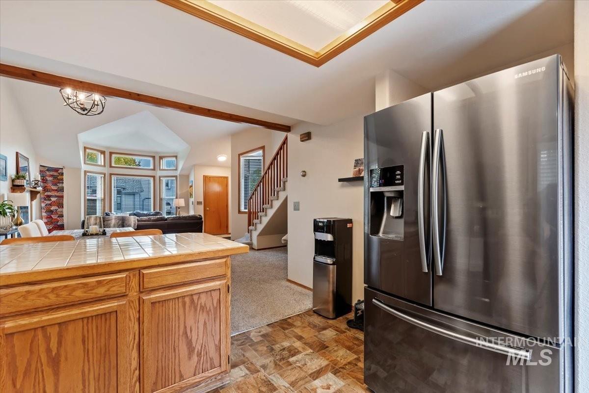 Kitchen with stainless steel fridge, open floor plan, tile counters, vaulted ceiling, and stone finish floors