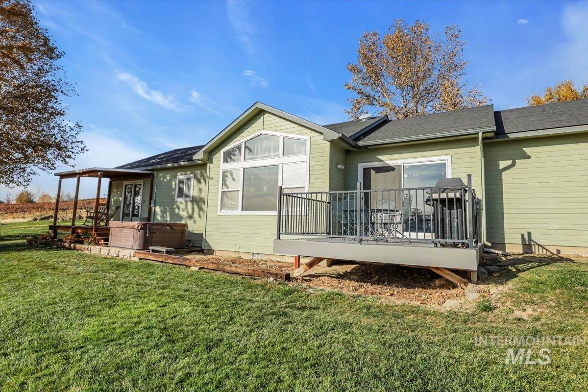 Rear view of house featuring a yard, roof with shingles, and a hot tub