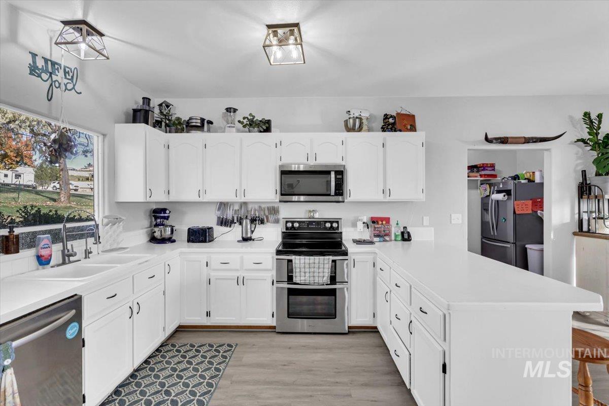 Kitchen featuring stainless steel appliances, white cabinets, a peninsula, light wood-style floors, and light countertops