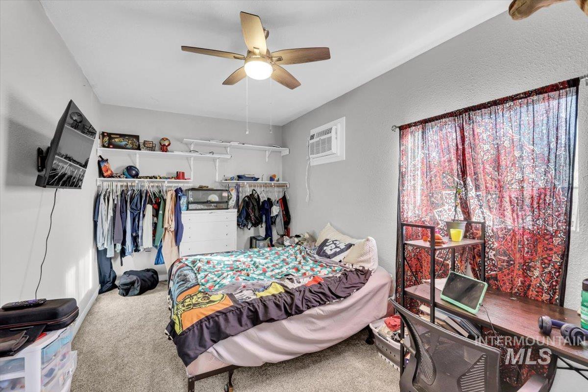 Carpeted bedroom featuring a textured wall, a ceiling fan, a closet, an AC wall unit, and a desk