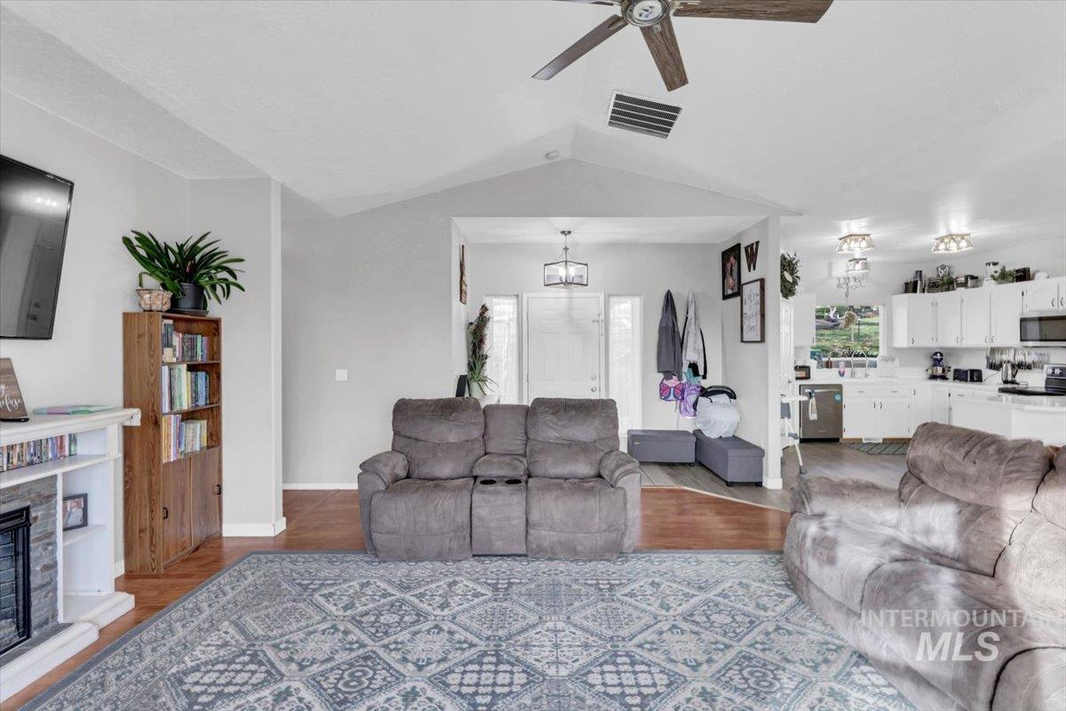 Living room featuring wood finished floors, lofted ceiling, ceiling fan, and a fireplace