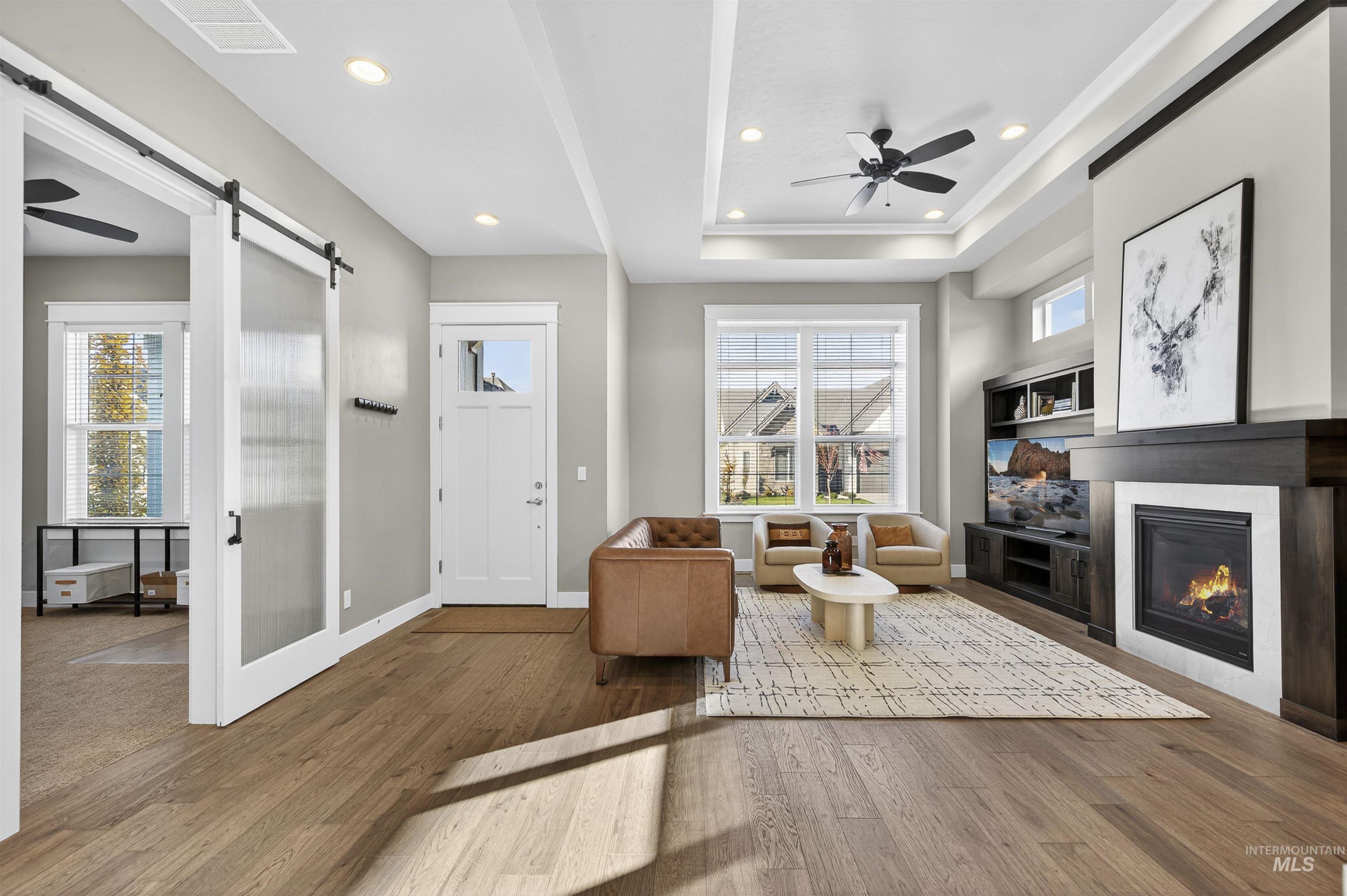 Living area featuring a ceiling fan, wood finished floors, a tray ceiling, a glass covered fireplace, and recessed lighting