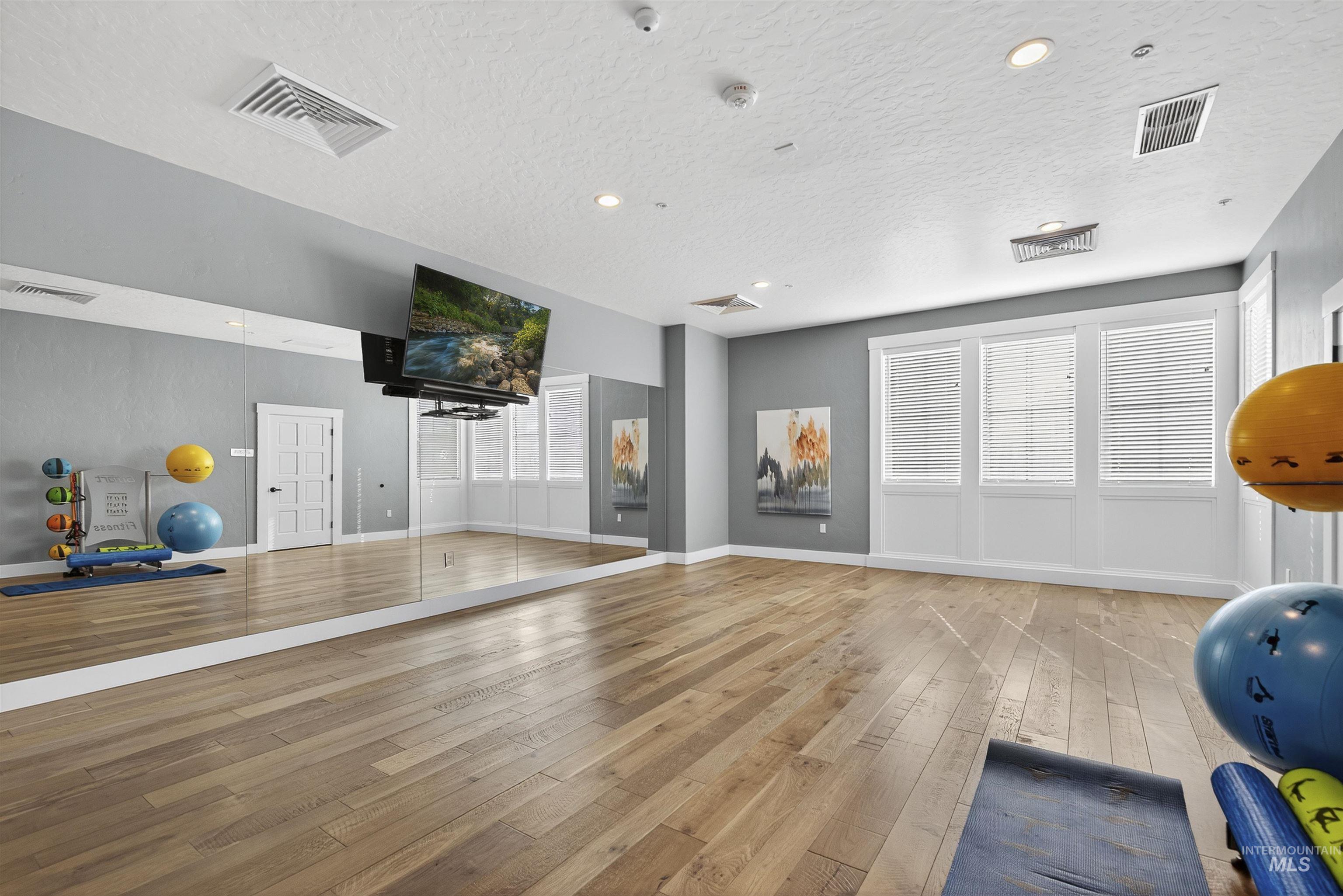 Exercise room featuring light wood-style floors, a textured ceiling, and recessed lighting