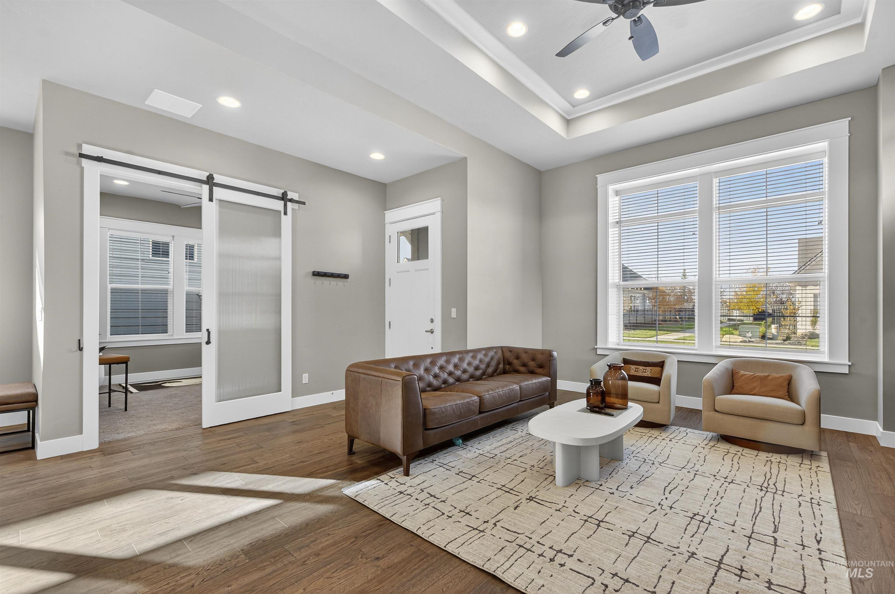 Living room with a barn door, a tray ceiling, recessed lighting, light wood-type flooring, and a ceiling fan
