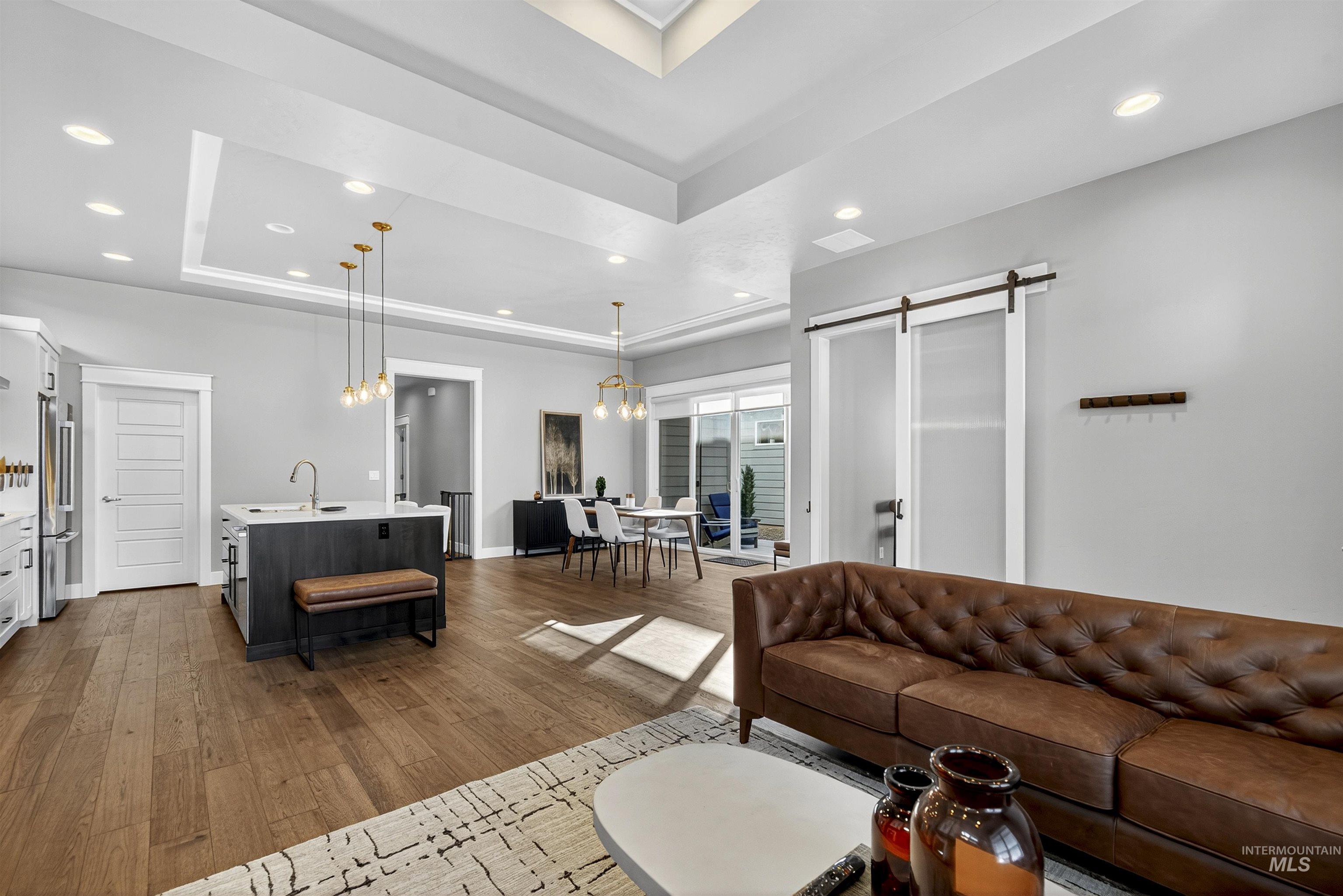 Living room featuring a tray ceiling, recessed lighting, dark wood finished floors, a barn door, and a chandelier