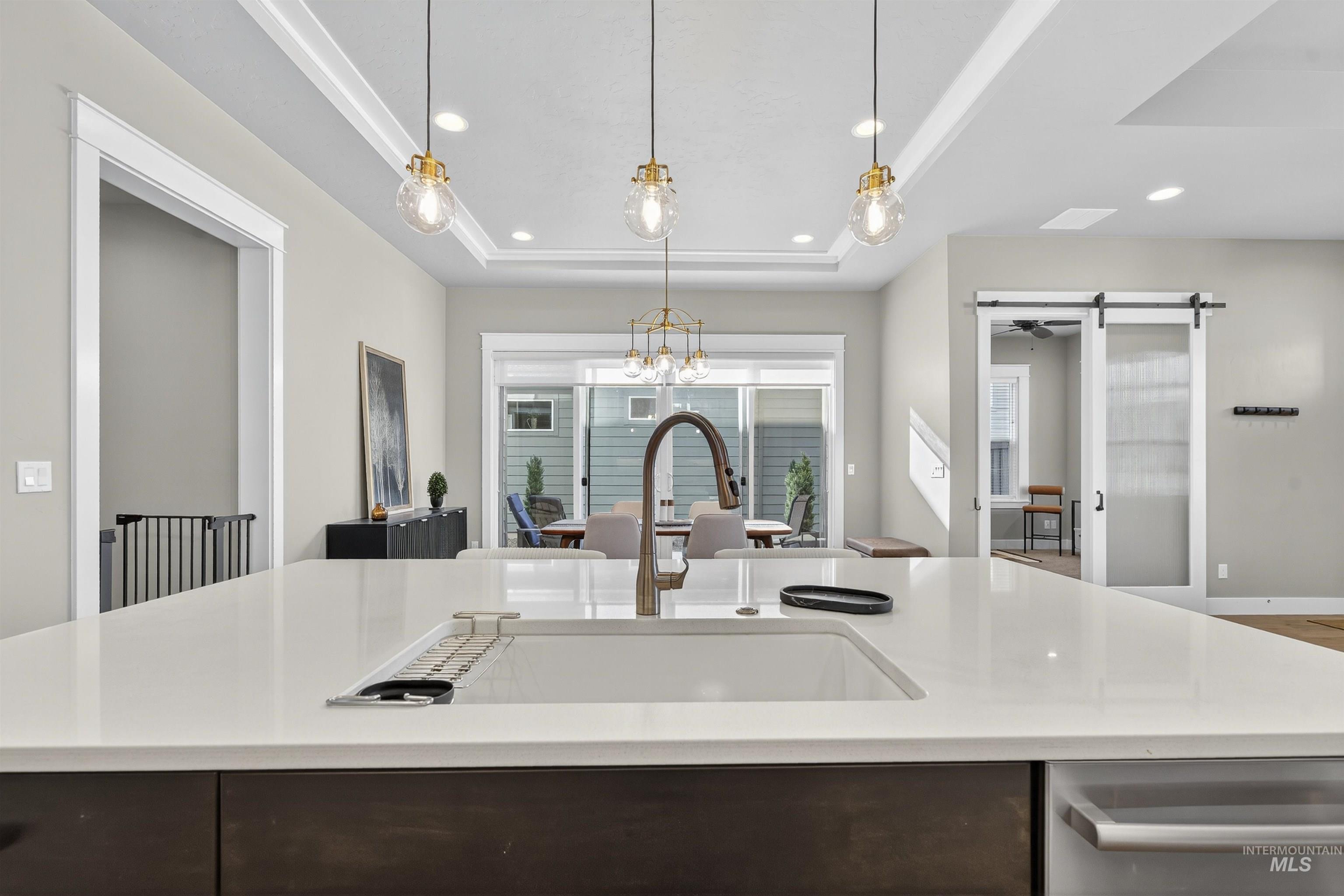 Kitchen featuring a tray ceiling, dark brown cabinetry, an island with sink, recessed lighting, and pendant lighting