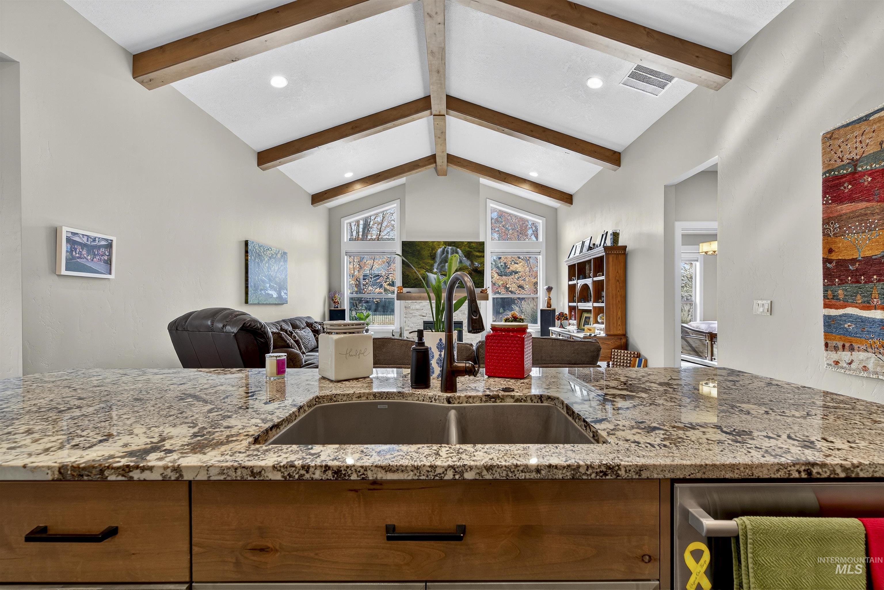 Kitchen featuring recessed lighting, brown cabinets, open floor plan, light stone countertops, and beam ceiling