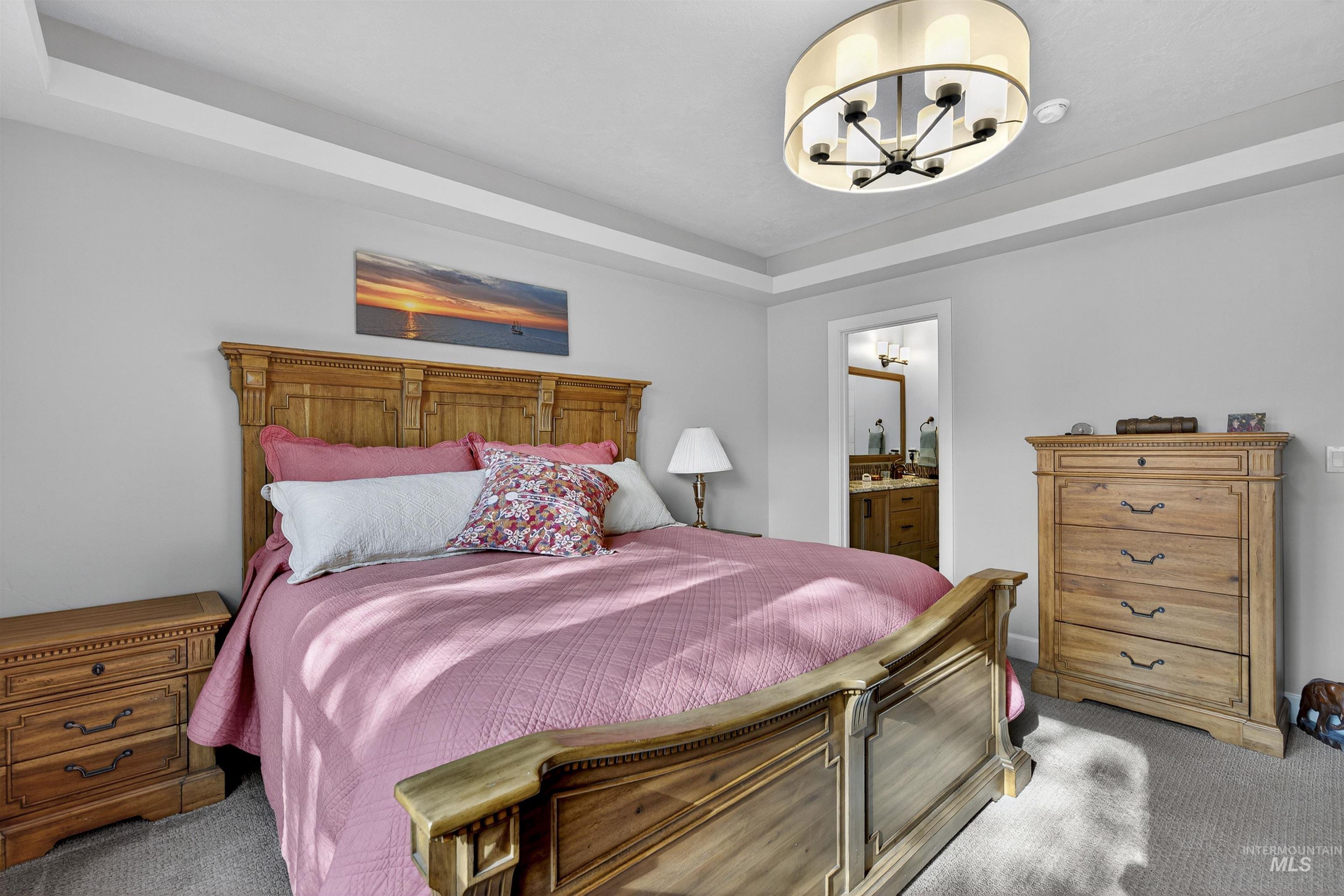 Bedroom featuring a raised ceiling, carpet flooring, ensuite bath, and a chandelier