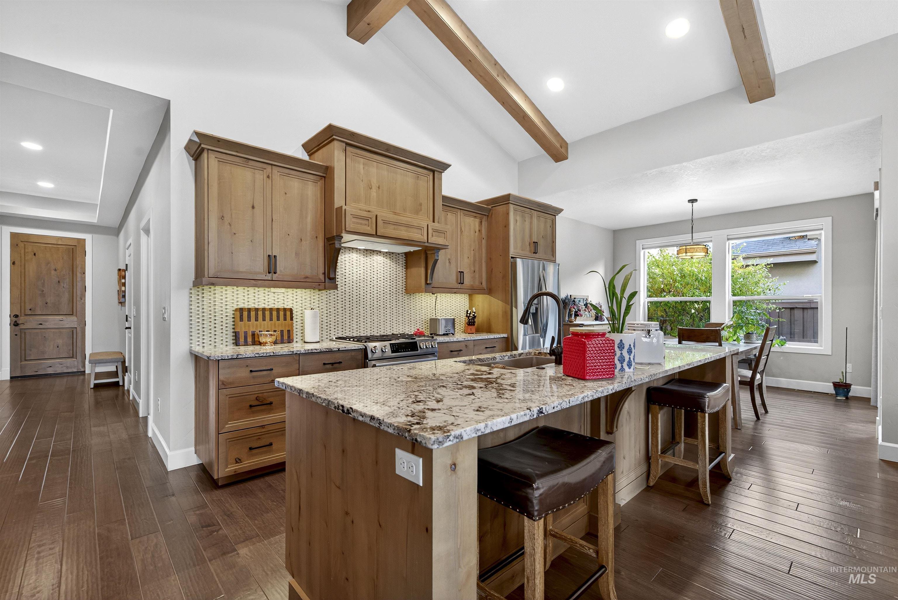 Kitchen featuring a breakfast bar area, light stone countertops, a center island with sink, tasteful backsplash, and dark wood-style floors