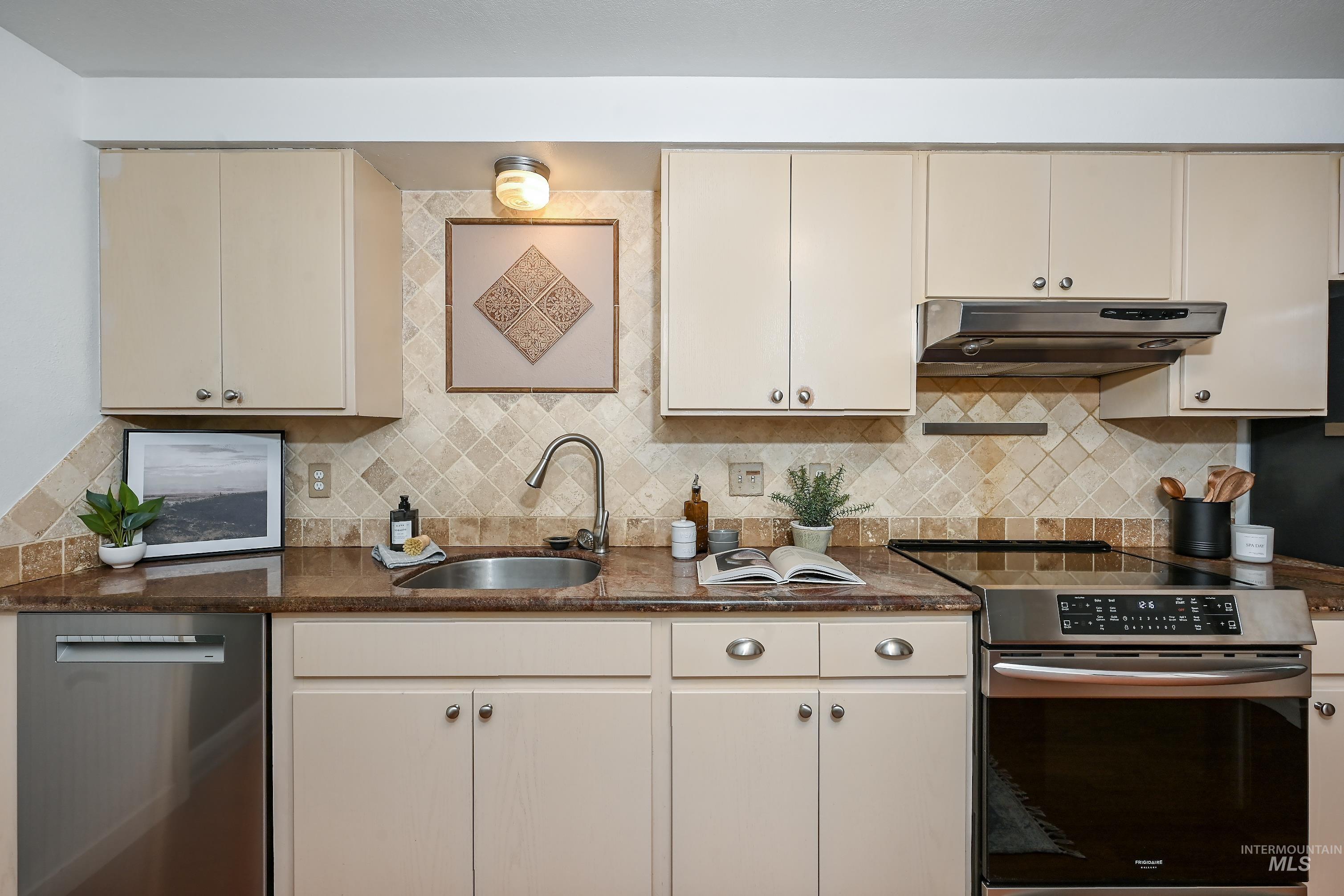 Kitchen with stainless steel appliances, backsplash, under cabinet range hood, and dark stone counters