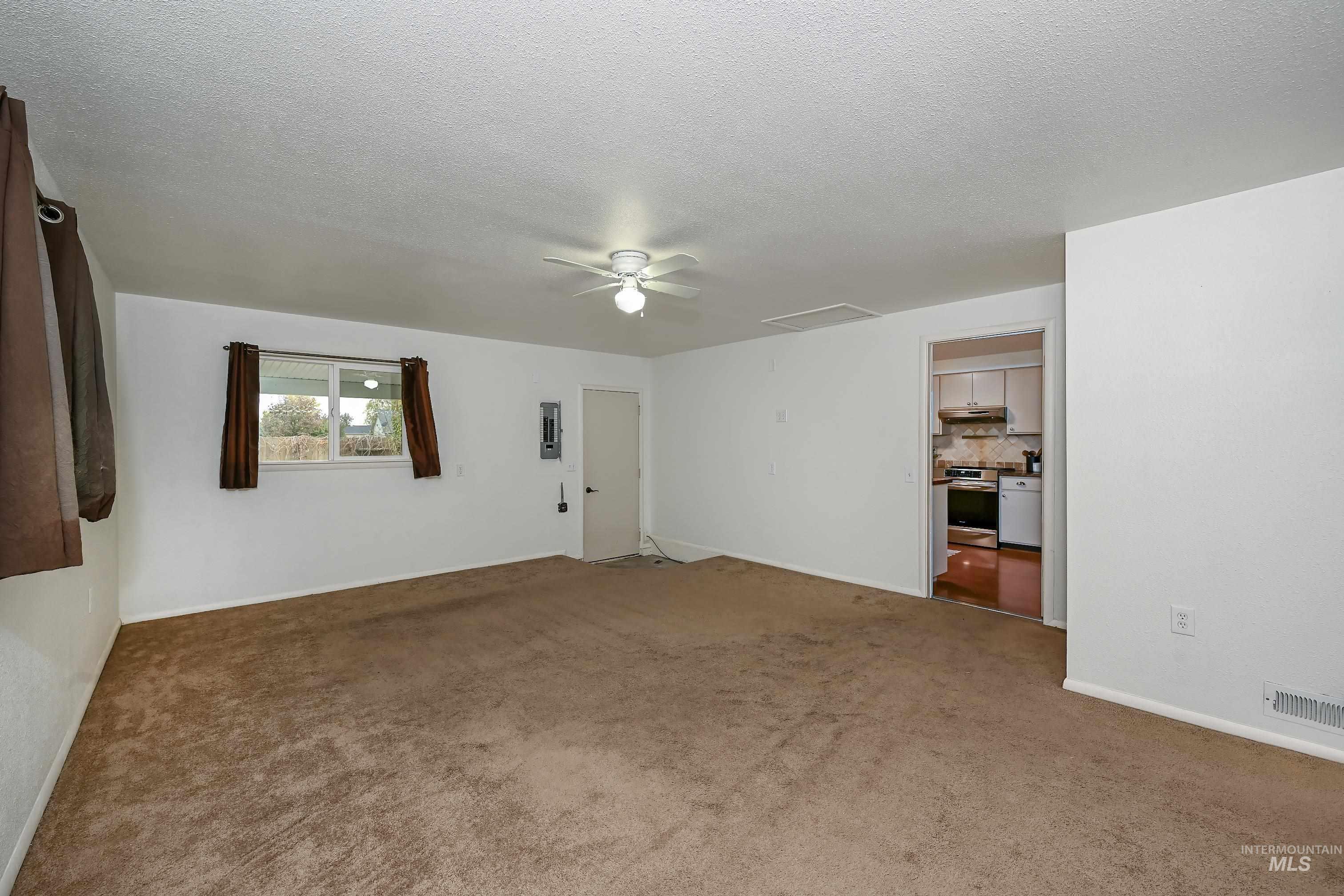 Carpeted empty room featuring a textured ceiling, a ceiling fan, and electric panel