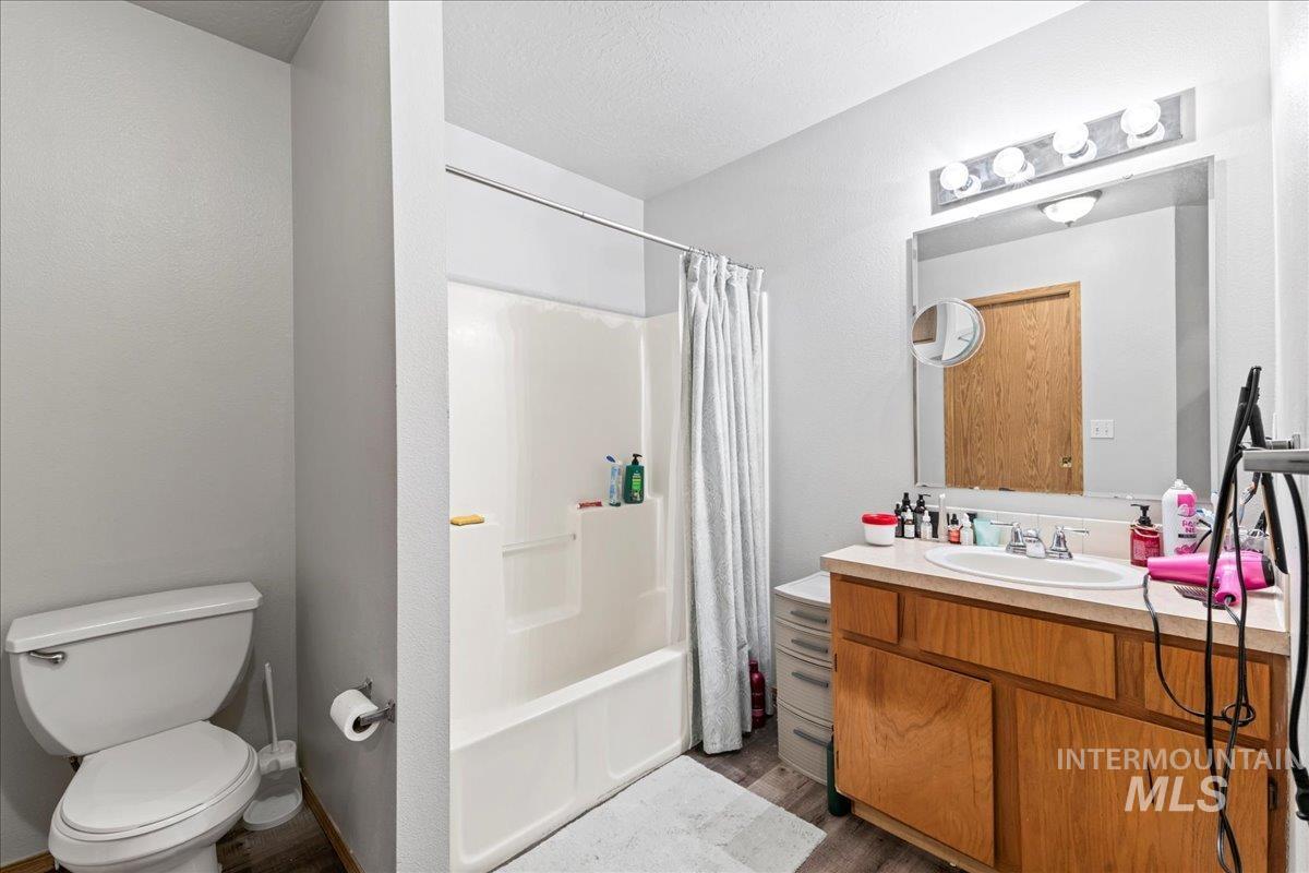 Full bath with vanity, shower / bath combo, dark wood-style flooring, and a textured ceiling