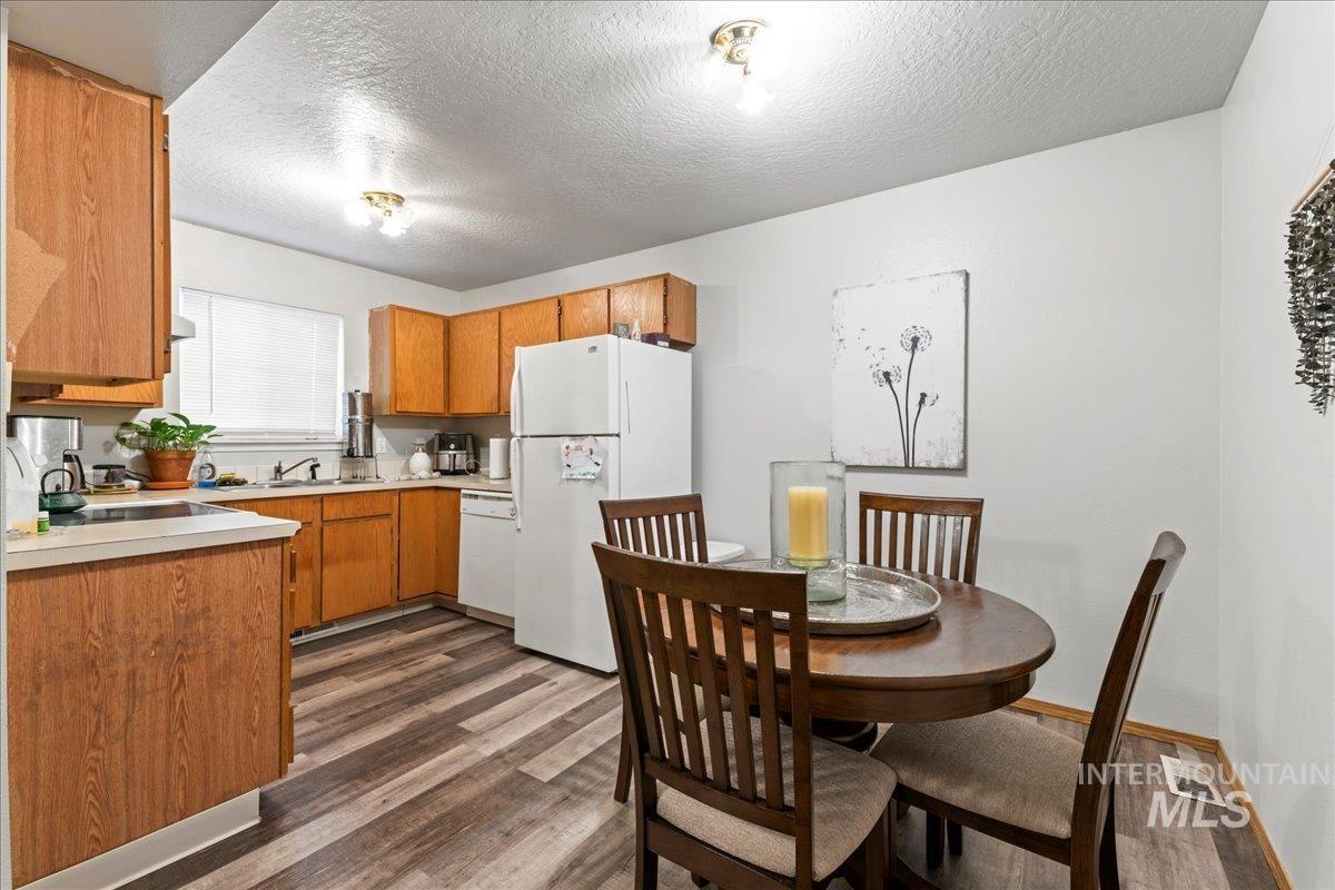 Kitchen featuring light countertops, brown cabinetry, white appliances, dark wood-style floors, and a textured ceiling