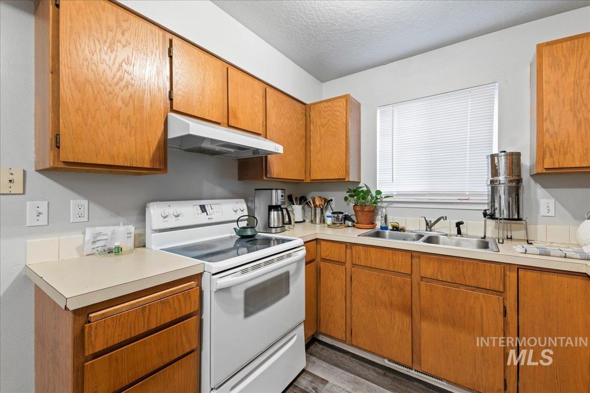 Kitchen with white range with electric stovetop, brown cabinets, under cabinet range hood, light countertops, and a textured ceiling