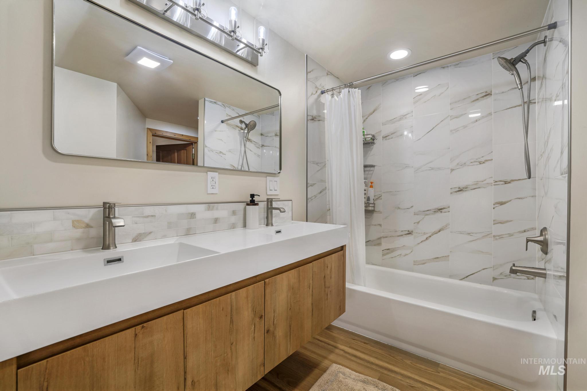 Bathroom featuring double vanity, a combined bath / shower with marble appearance, dark wood-type flooring, recessed lighting, and tasteful backsplash