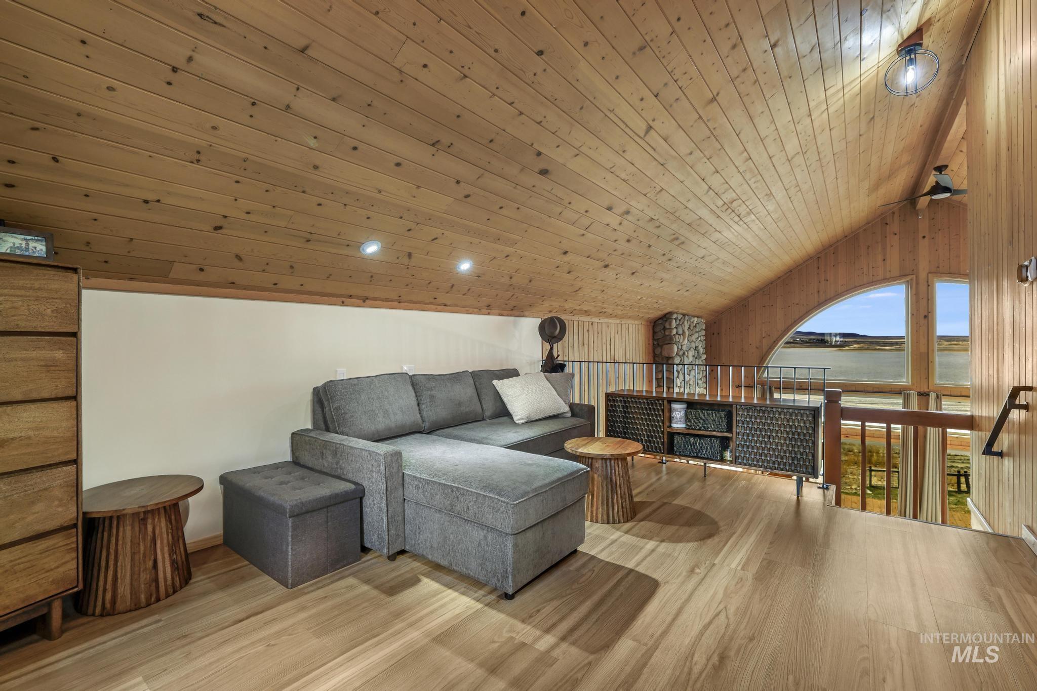 Living area with lofted ceiling, wood ceiling, light wood-type flooring, a water view, and an upstairs landing