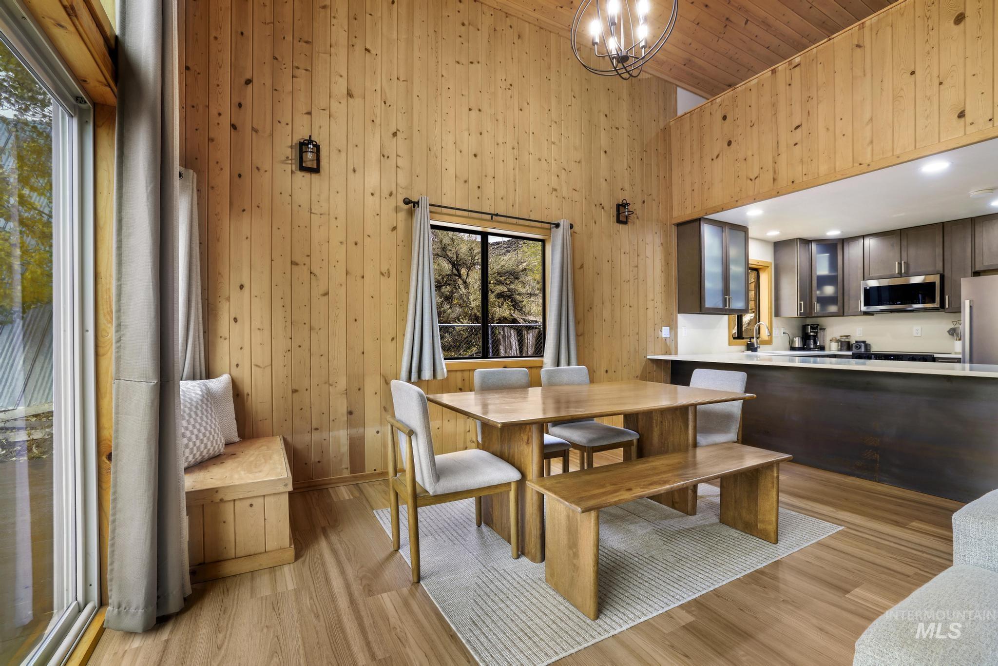 Dining space with light wood-style floors, wooden walls, a towering ceiling, and wood ceiling