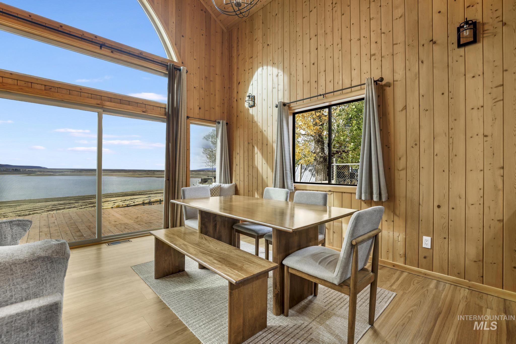 Dining area featuring a water view, wooden walls, a high ceiling, and wood finished floors