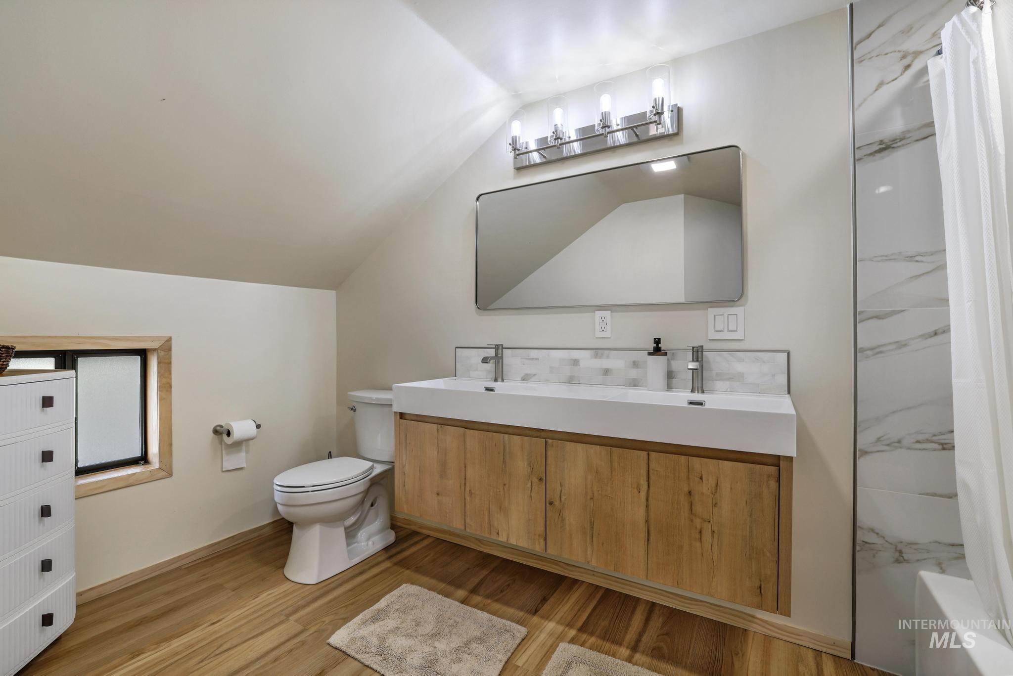 Full bathroom with vaulted ceiling, double vanity, light wood finished floors, and shower / bath combination with curtain