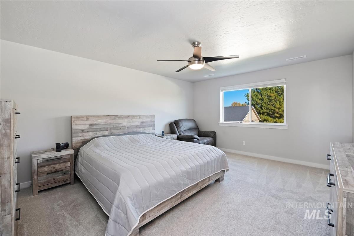 Bedroom with light carpet, a ceiling fan, and a textured ceiling
