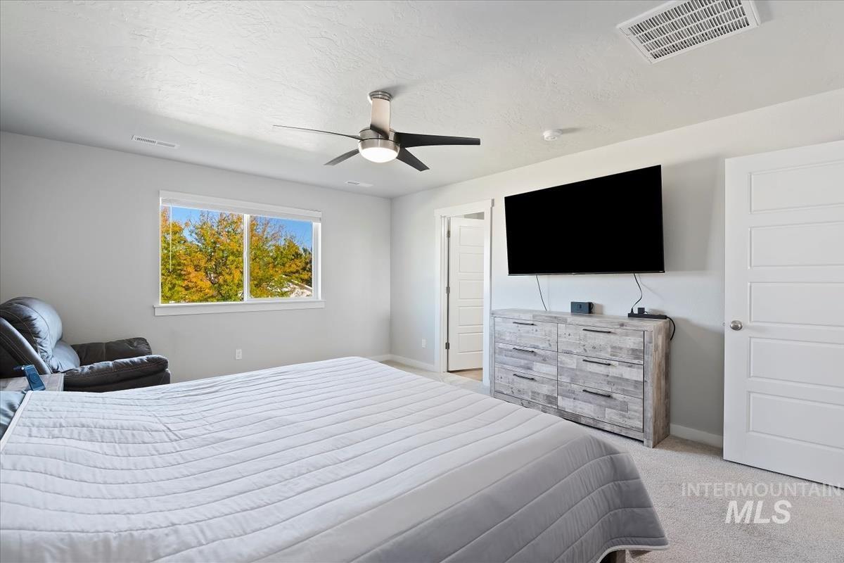 Bedroom with light colored carpet, ceiling fan, and a textured ceiling
