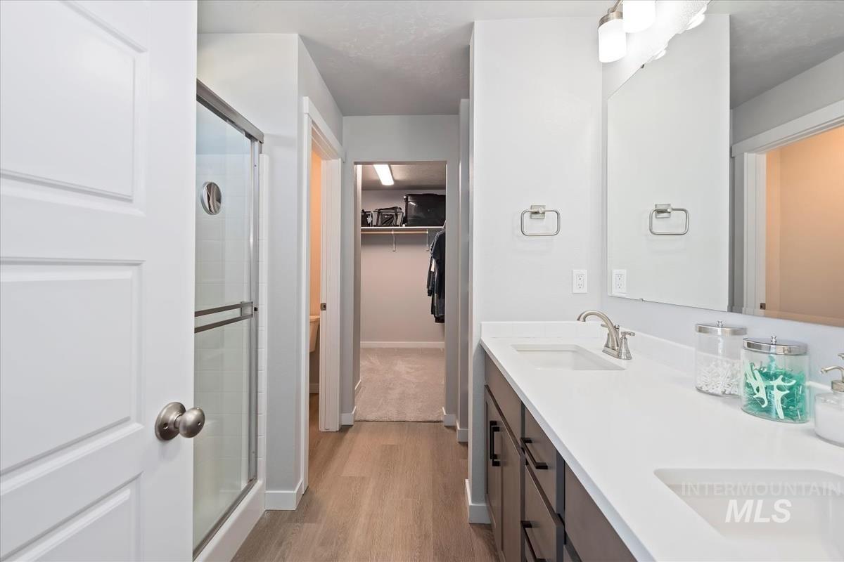 Bathroom featuring double vanity, light wood-style floors, a walk in closet, and a stall shower