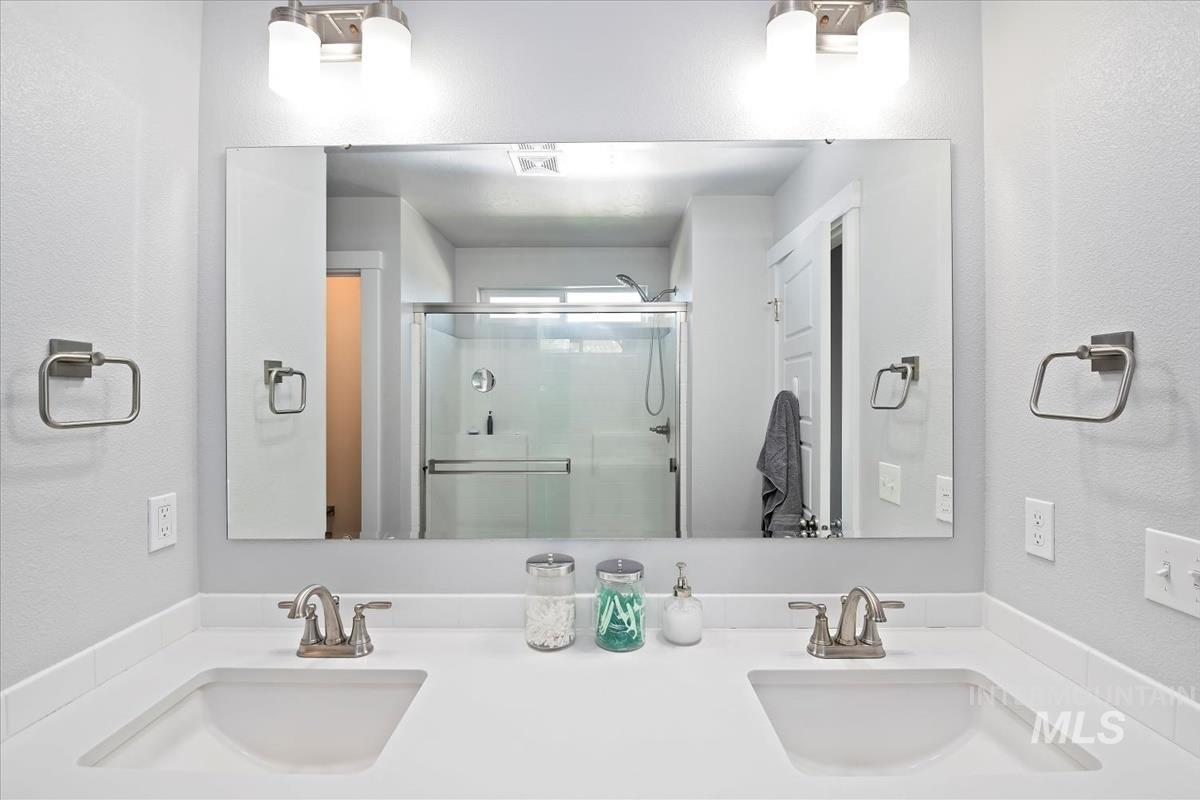 Full bath featuring a textured wall, double vanity, and a shower stall