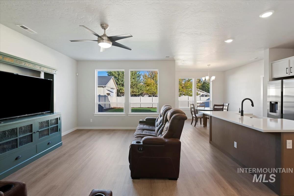 Living area featuring light wood-type flooring, a chandelier, ceiling fan, and a textured ceiling